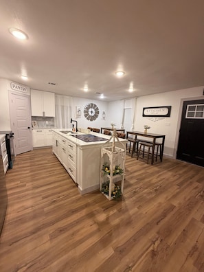 A kitchen with white cabinetry, a central island, a dining area with a table and chairs, and a black door. - The Rustic Charm- Downtown Midlothian- Full House (Midlothian)