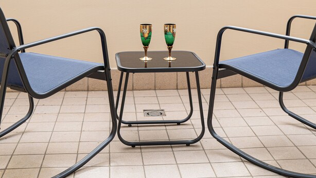 Een terras met twee stoelen en een kleine tafel, een gebouw met boogvensters en baksteen op de achtergrond.