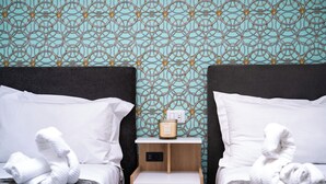 Een hotelkamer met twee bedden, een nachtkastje met een lamp en een muur met een geometrisch patroon.
