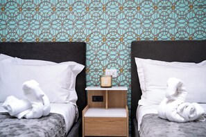 A hotel room with two beds, a nightstand with a lamp, and a wall with a geometric pattern. - Florence Dream Homes - Medusa (Firenze Fl)