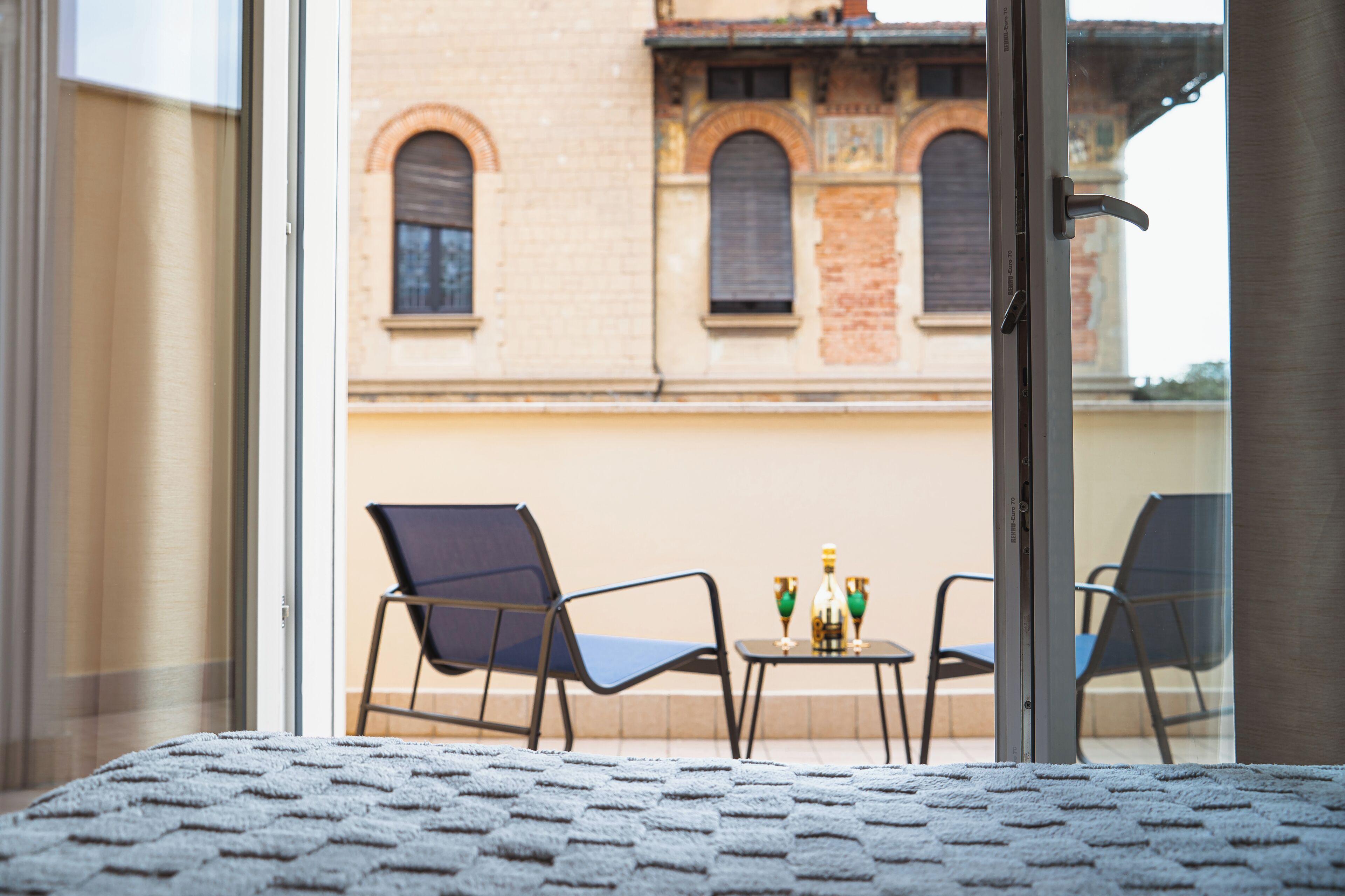 A balcony with two chairs and a small table, overlooking a building with arched windows.