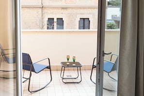 Ein Balkon mit zwei Stühlen, einem kleinen Tisch und einer Glastür, im Hintergrund ein Gebäude.