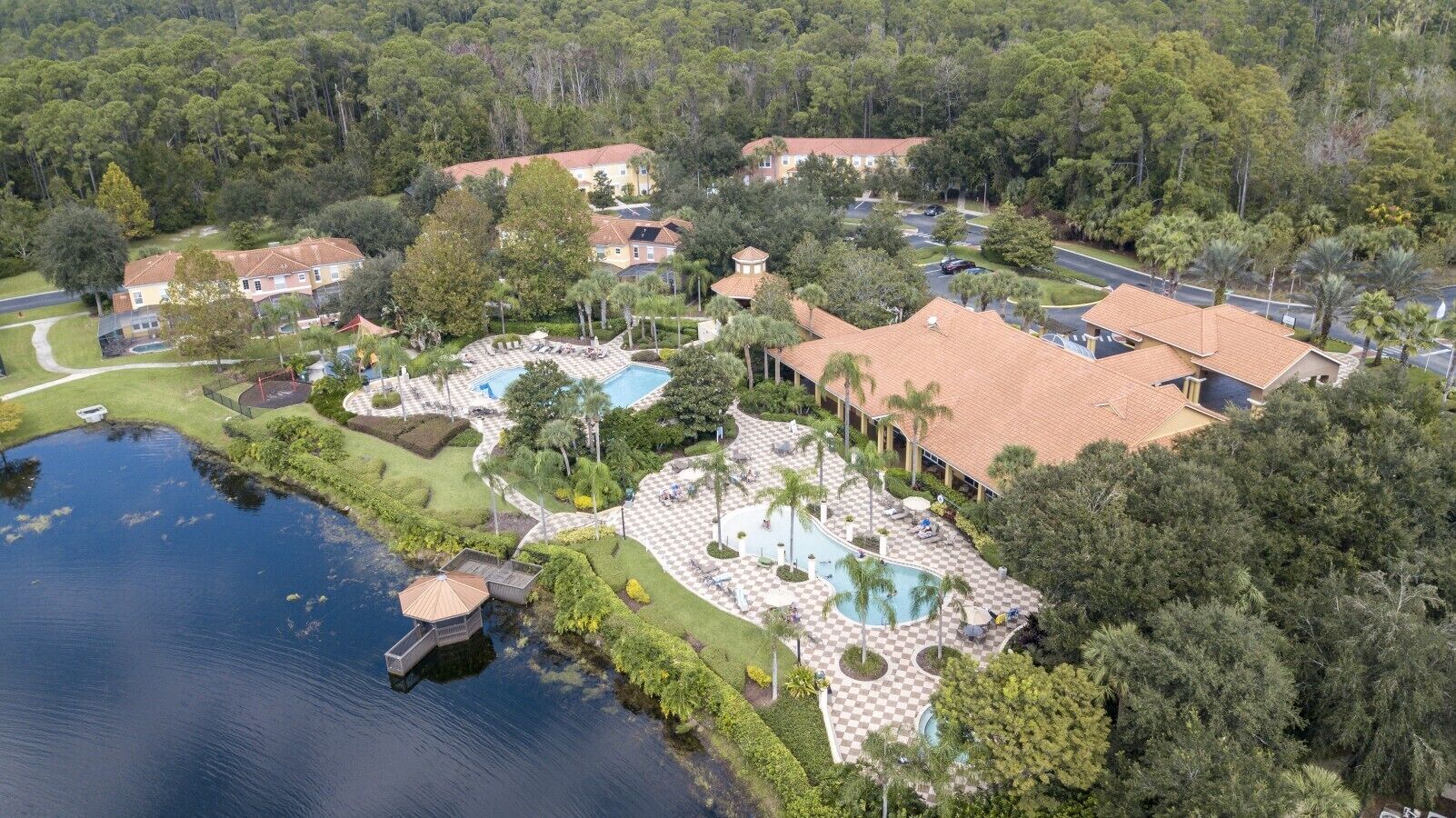 A residential area with a swimming pool, a tennis court, and a large house surrounded by trees.