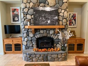 A stone fireplace with a picture above it, a television on a stand to the left, and a wooden cabinet with drawers to the right. - River Villa with pool and spa ~ Best Swimming Hole (Three Rivers)