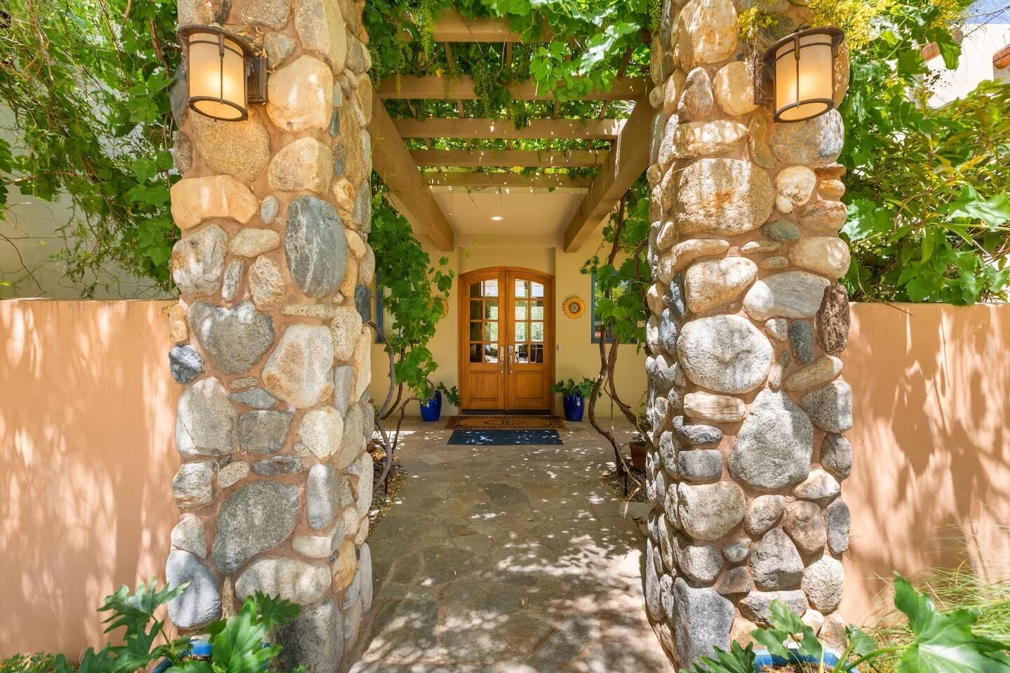 Un arco de piedra que conduce a una puerta de madera, rodeado de follaje y muros de piedra.