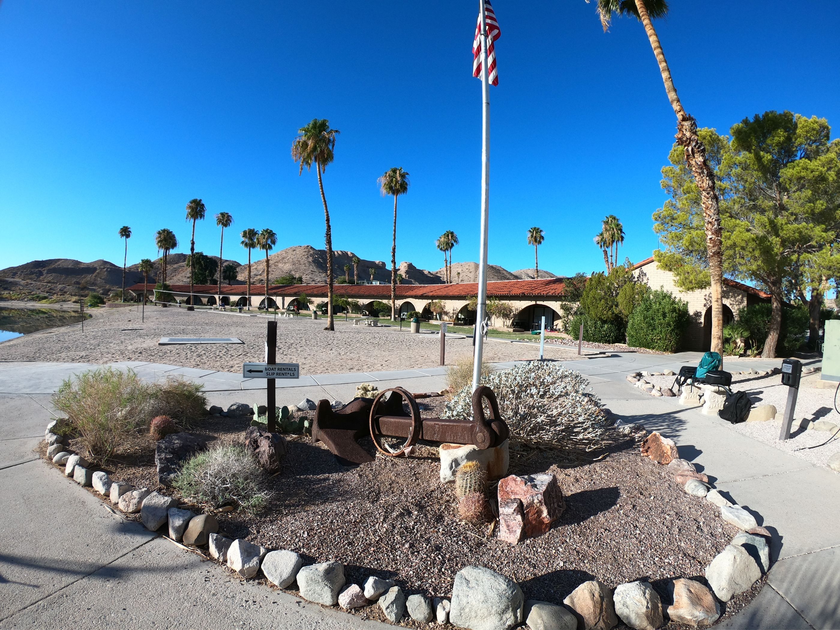 A desert landscape with a historic building, palm trees, and a cannon in the foreground.