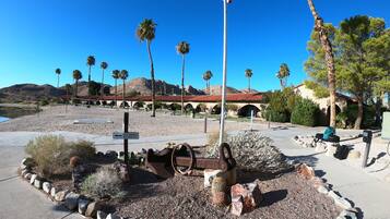 A desert landscape with a historic building, palm trees, and a cannon in the foreground.