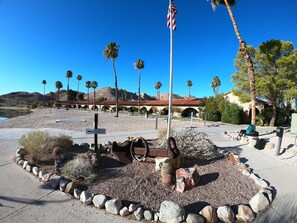 A desert landscape with a historic building, palm trees, and a cannon in the foreground.