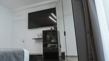 A bedroom with a bed, a wardrobe, a television mounted on the wall, and a small shelf with items.