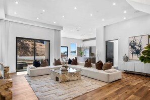 Ein modernes Wohnzimmer mit einem Ecksofa, einem Glastisch und Blick auf eine angelegte Grünfläche durch große Schiebetüren.