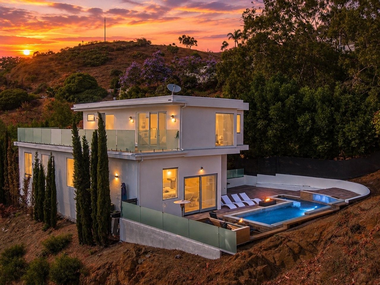 Una casa moderna de dos pisos con piscina y vistas al atardecer.