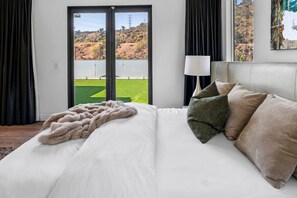 Een slaapkamer met een bed, uitzicht op een groen veld door een schuifdeur en een lamp op een nachtkastje.