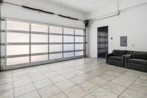 A spacious garage with a large garage door, tiled floor, and a sofa in the corner. - ৎ୭Luxury Hollywood Hills | 5BR + Poolৎ୭ (Los Angeles)