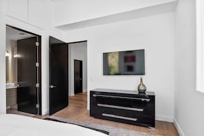 Ein modernes Schlafzimmer mit einem großen Bett, einer dunklen Holzkommode, einem flachbildfernseher an der Wand und einem Flur, der in einen anderen Raum führt.