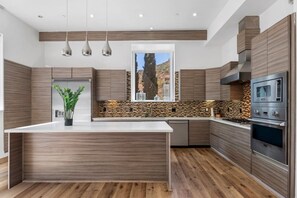 Een moderne keuken met een centraal eiland, inbouwapparatuur en uitzicht op een bergachtig landschap.