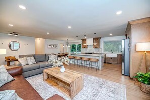 A modern living room with a sofa, coffee table, and a kitchen area with bar stools. - North Hills Raleigh Retreat (Raleigh)
