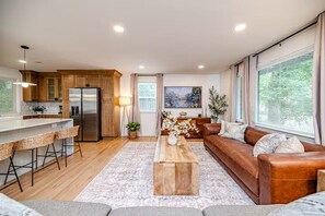 Un salon moderne comprenant un canapé, une table basse et un coin cuisine avec des meubles en bois et un réfrigérateur.