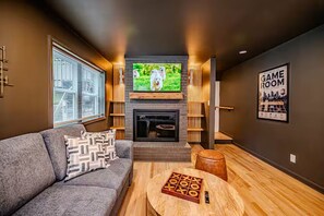 A living room with a fireplace, a television mounted above it, a sofa with patterned cushions, and a wooden coffee table. - North Hills Raleigh Retreat (Raleigh)