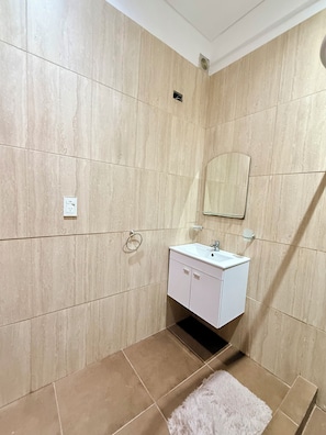 A bathroom with a white sink, mirror, and beige tiled walls.