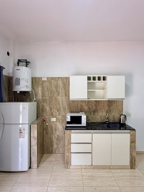 A compact kitchen with a built-in refrigerator, a microwave, and a kettle on the countertop.