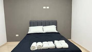 A neatly made bed with a black bedspread and white pillows, accompanied by rolled white towels.