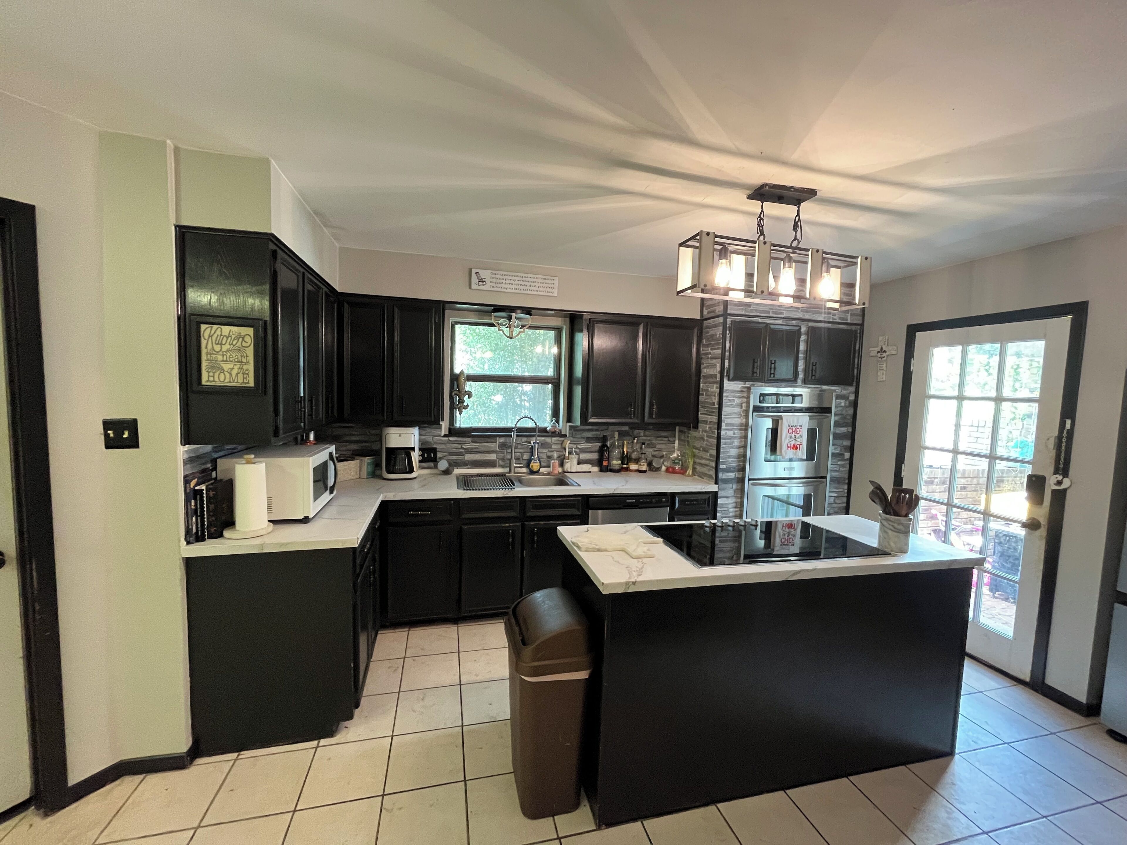A modern kitchen with dark cabinetry, a central island, a built-in oven, and a window providing natural light.