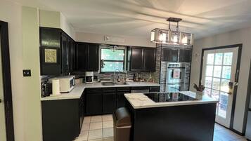 A modern kitchen with dark cabinetry, a central island, a built-in oven, and a window providing natural light.