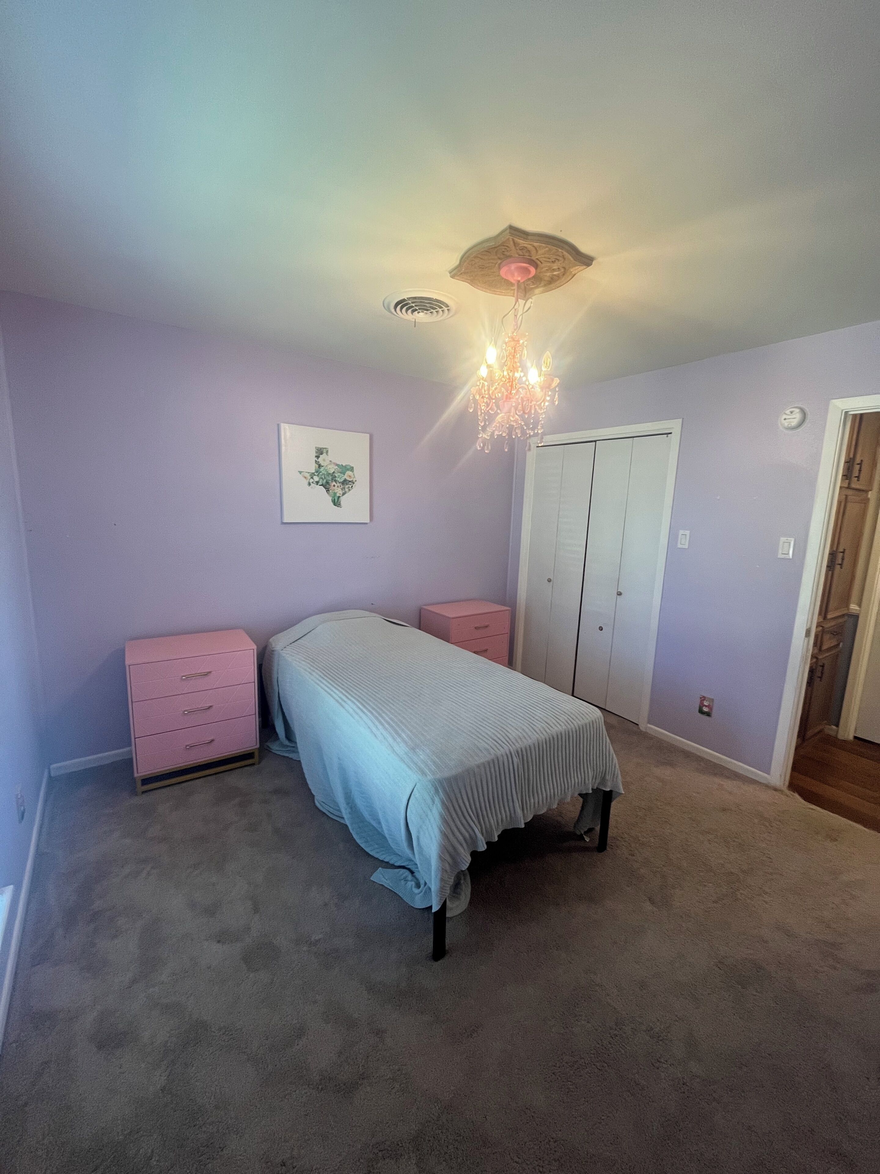 A bedroom with a bed, a dresser, a nightstand, a chandelier, and a door.