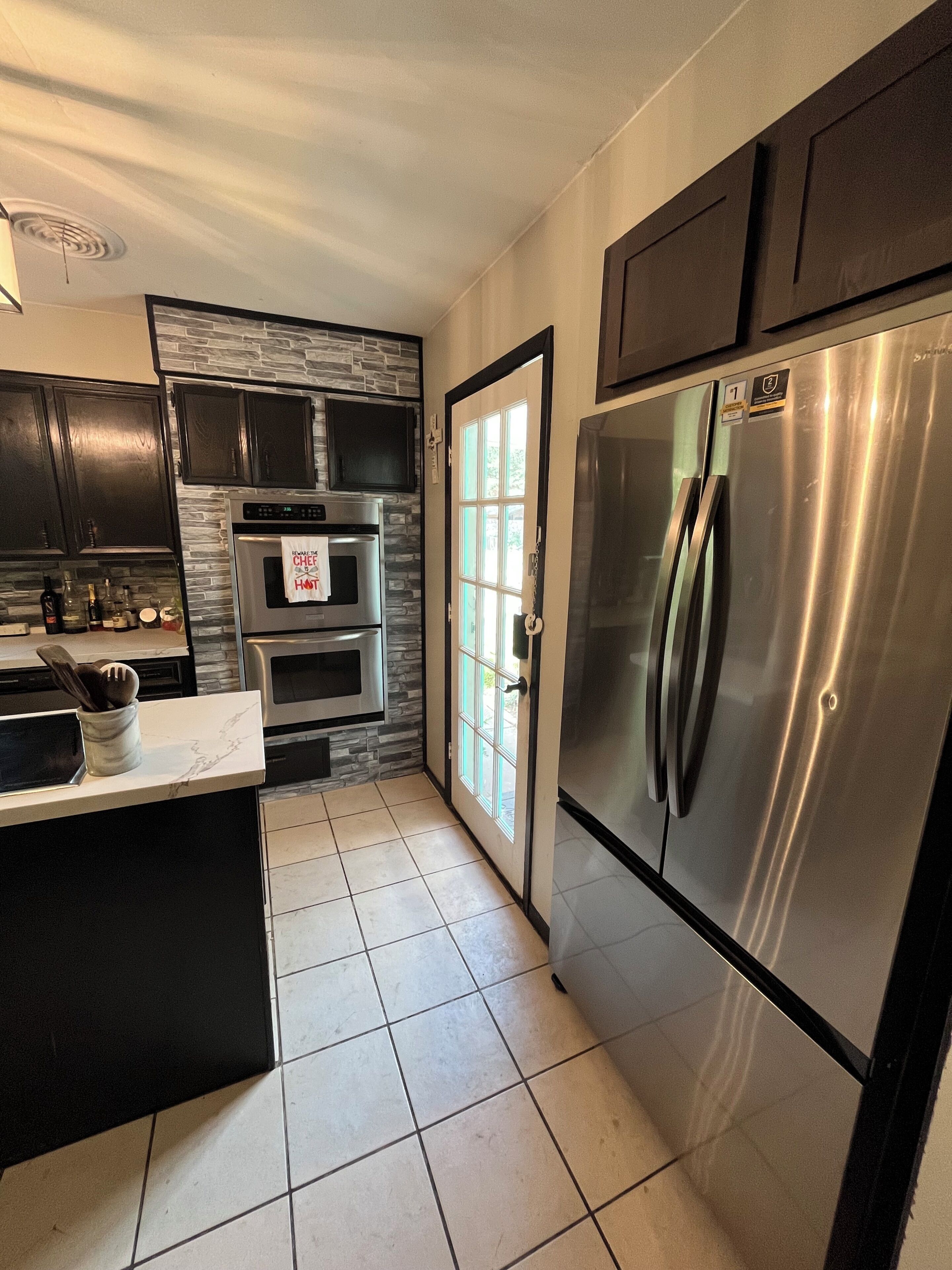 A modern kitchen with a stainless steel refrigerator, a built-in oven, and a stone backsplash.