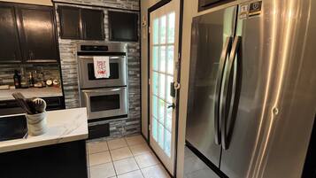 A modern kitchen with a stainless steel refrigerator, a built-in oven, and a stone backsplash.