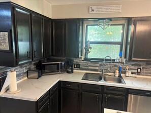 A kitchen with dark cabinets, a microwave, a coffee maker, and a window with a view of greenery.