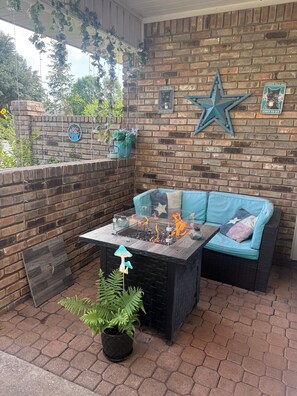 A patio area with a brick wall, a star decoration, a fire pit table, and a blue sofa.