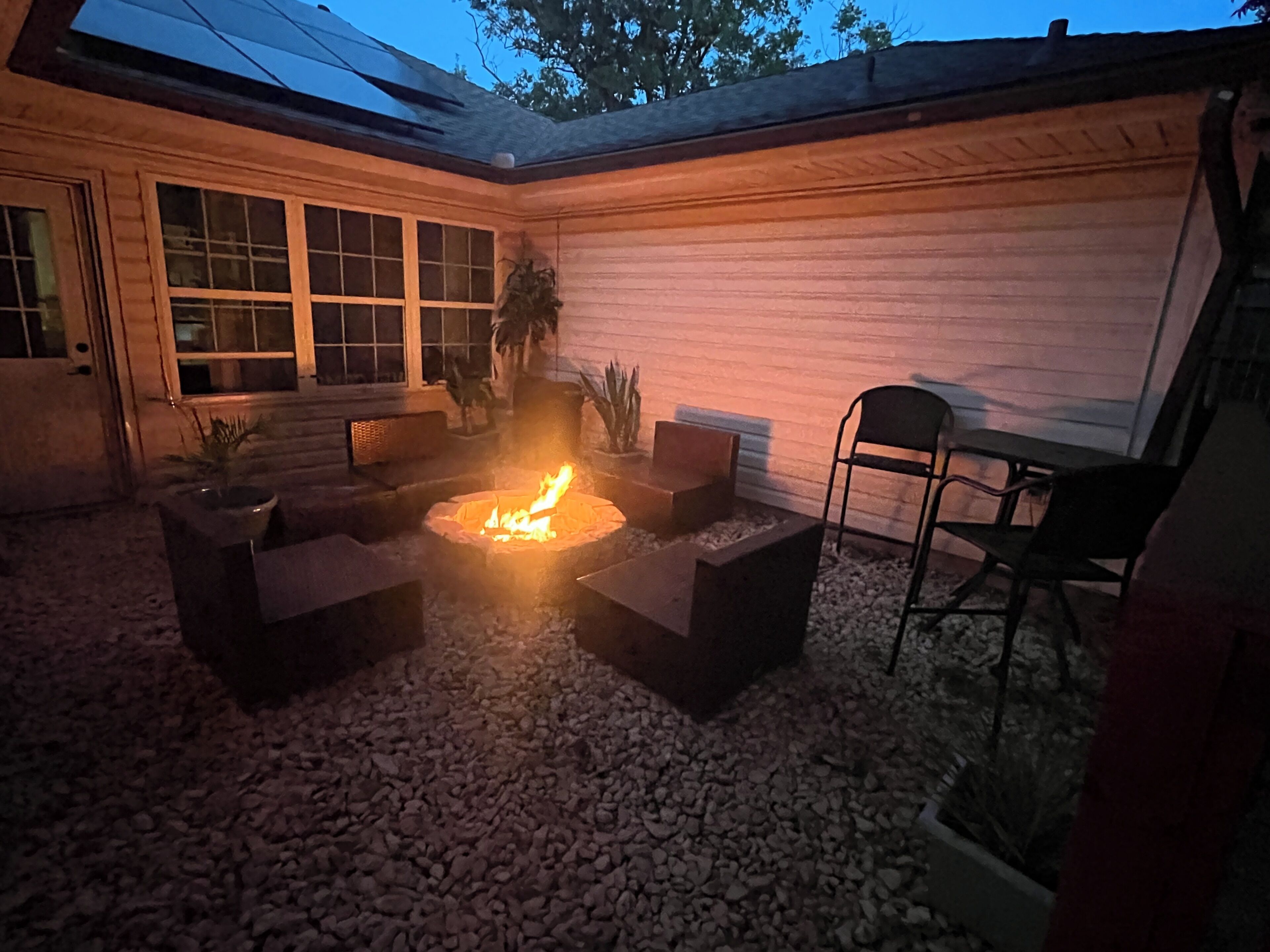 An outdoor patio area with a fire pit, seating, and a view of the house.