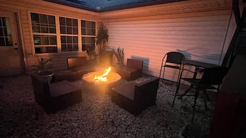 An outdoor patio area with a fire pit, seating, and a view of the house.