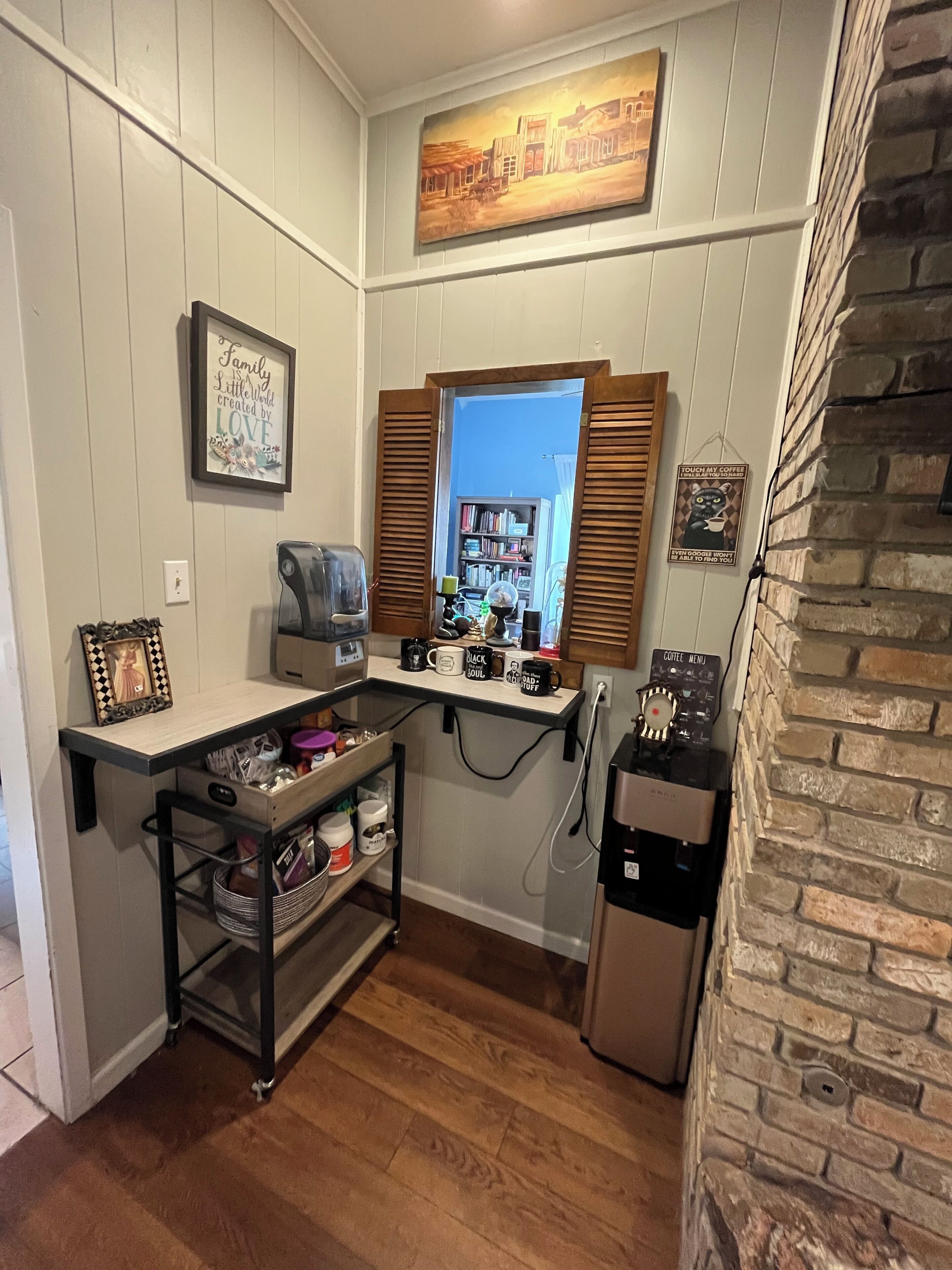 Una cocina compacta con estación para café, una estantería y una ventana con contraventanas.