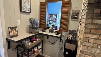 Una cocina compacta con estación para café, una estantería y una ventana con contraventanas.