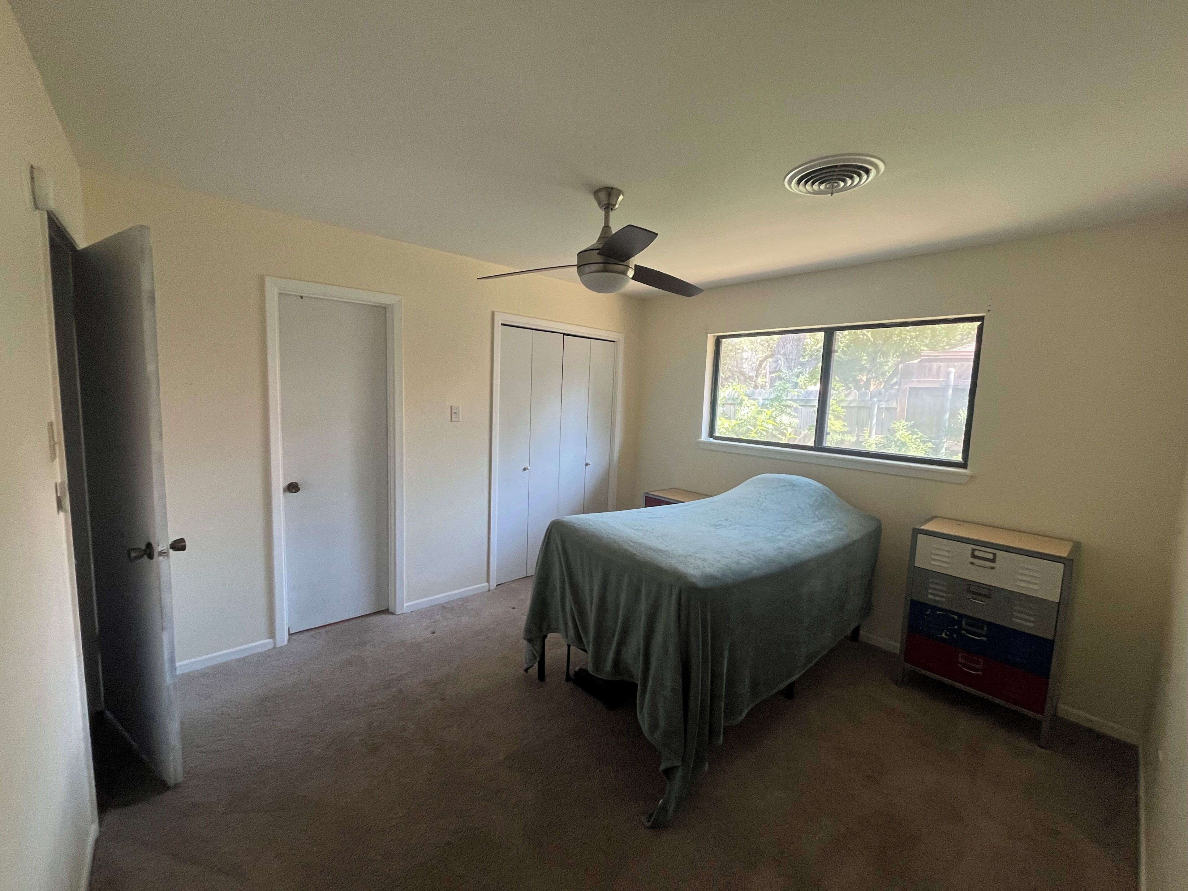 A bedroom with a bed, a ceiling fan, a window, and a dresser.