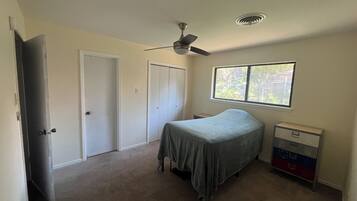 A bedroom with a bed, a ceiling fan, a window, and a dresser.