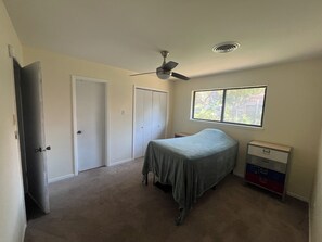 Ein Schlafzimmer mit Bett, Deckenventilator, Fenster und Kommode.