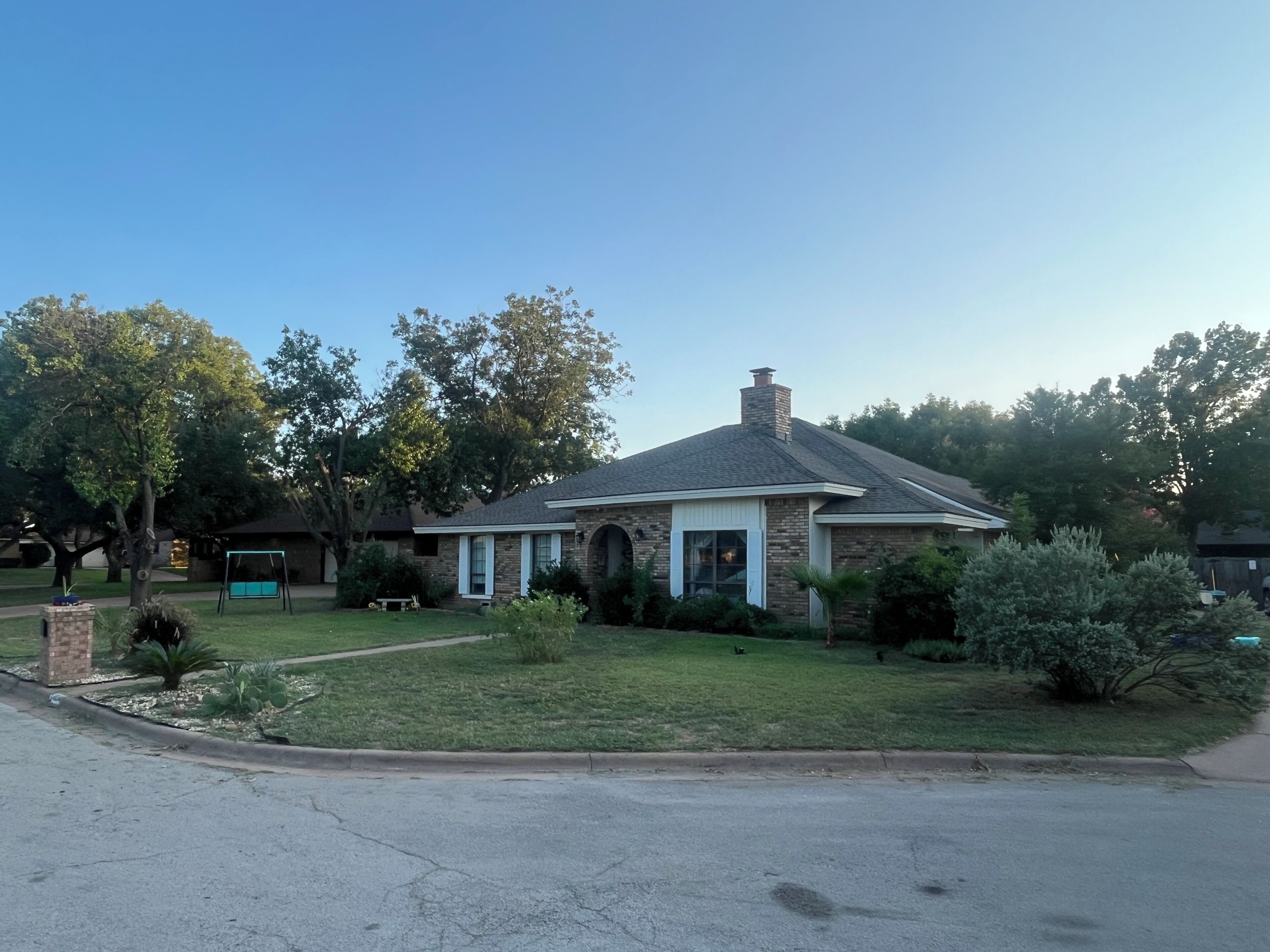 A residential house with a brick exterior, a front porch, and a lawn.