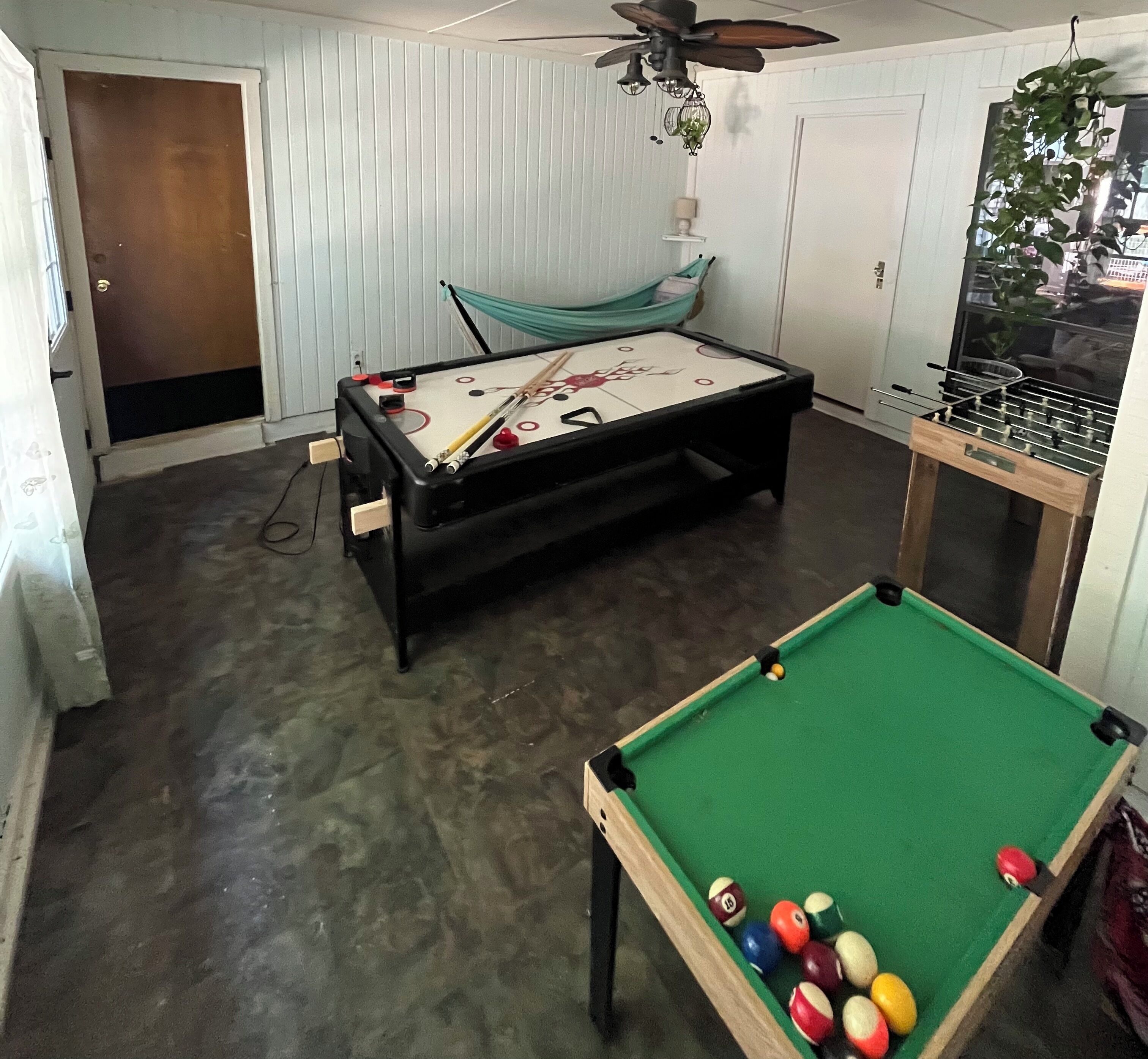 Uma sala com mesa de bilhar, mesa de pebolim e rede para descanso.