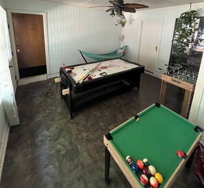 A room with a pool table, a foosball table, and a hammock.