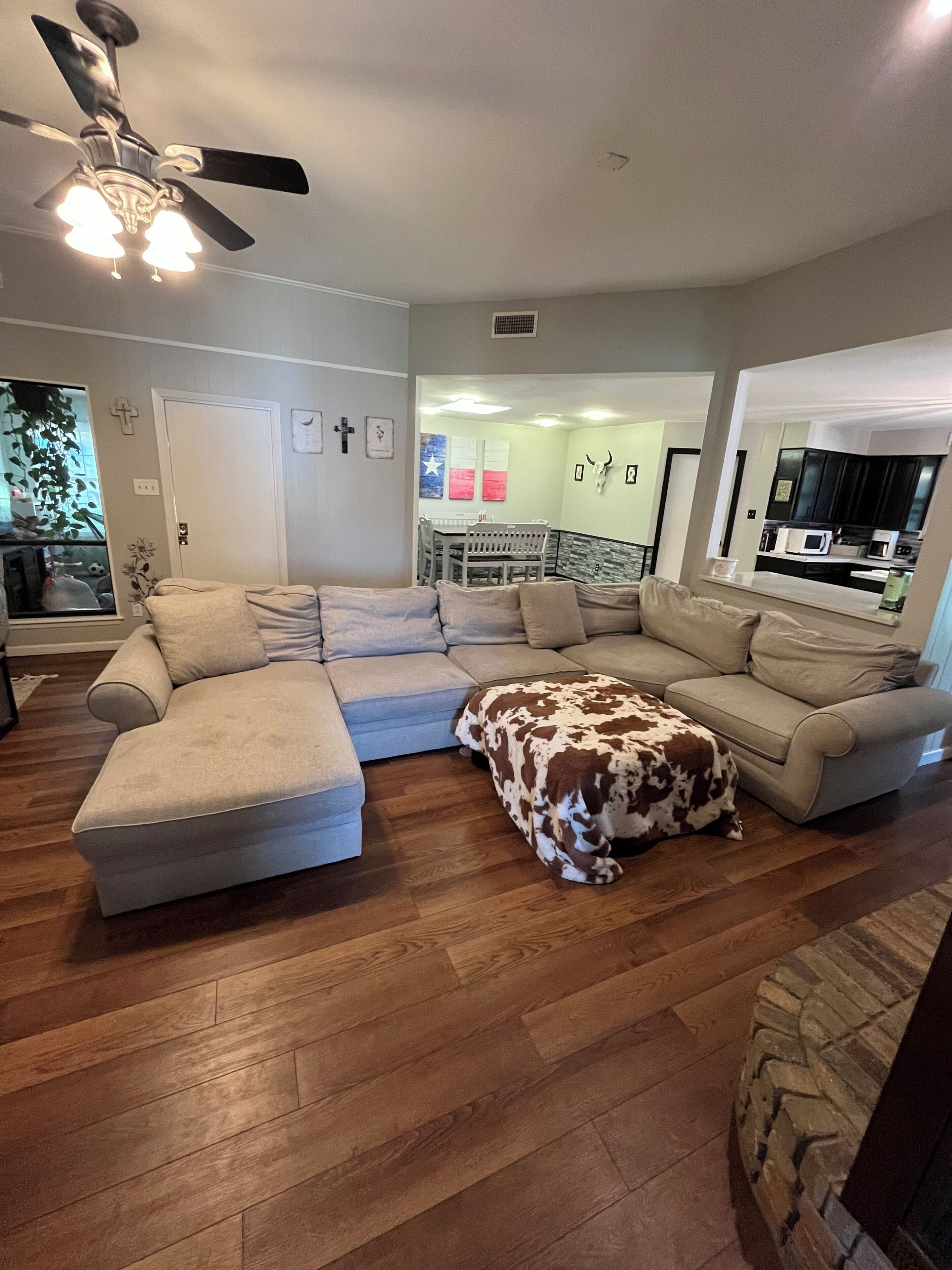 A living room with a sectional sofa, ottoman, and ceiling fan.