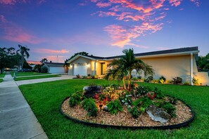 A residential house with a well-maintained lawn and a circular garden bed with various plants and flowers. - Clearwater Waterfront Escape w/ Private Pool (Clearwater)