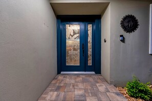 A blue door with a frosted glass panel, a small wall-mounted light, and a decorative sunburst on the wall. - Clearwater Waterfront Escape w/ Private Pool (Clearwater)
