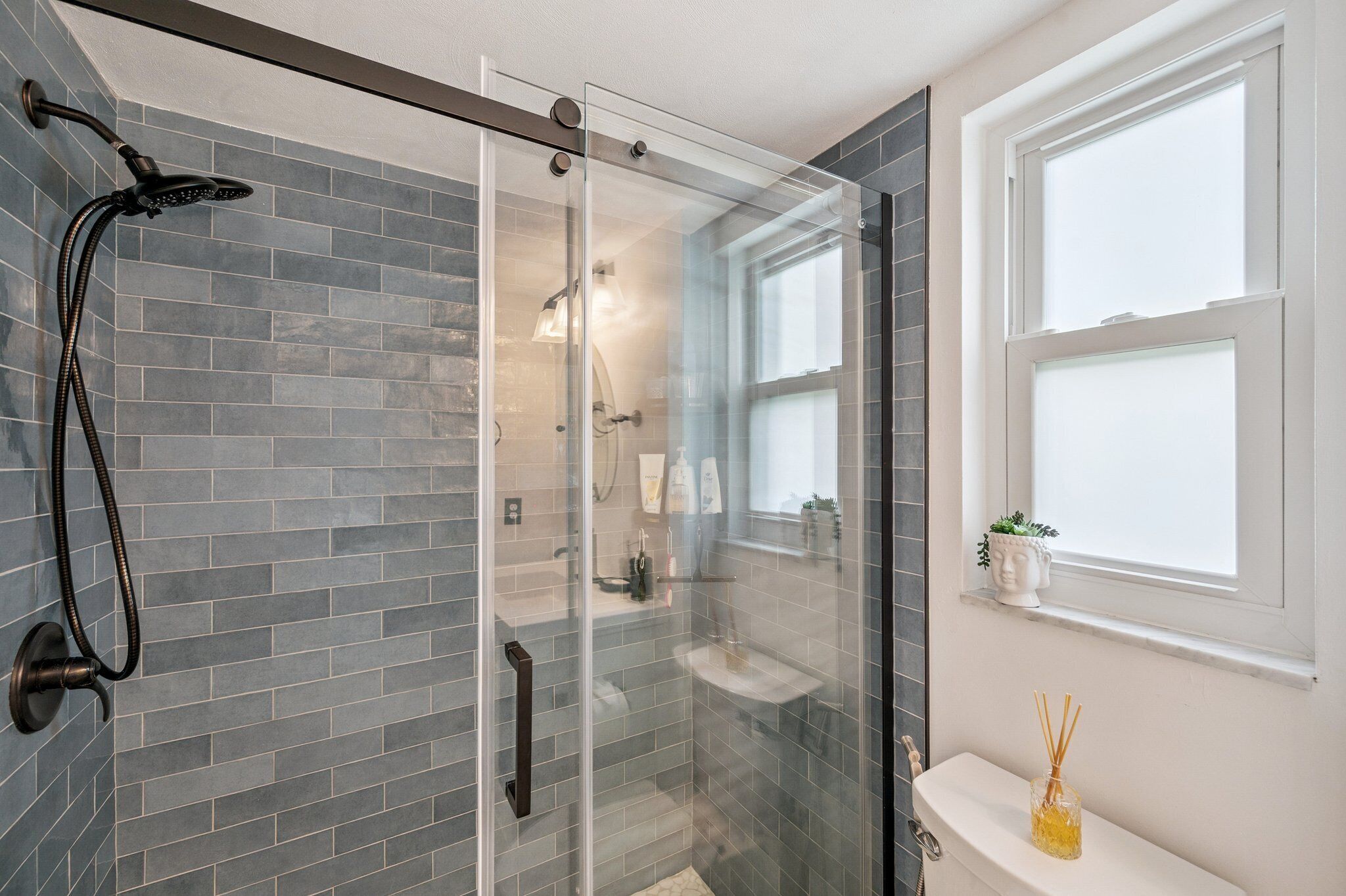 Een moderne badkamer met een glazen douchecabine, een witte wastafel en een raam voor natuurlijk licht.
