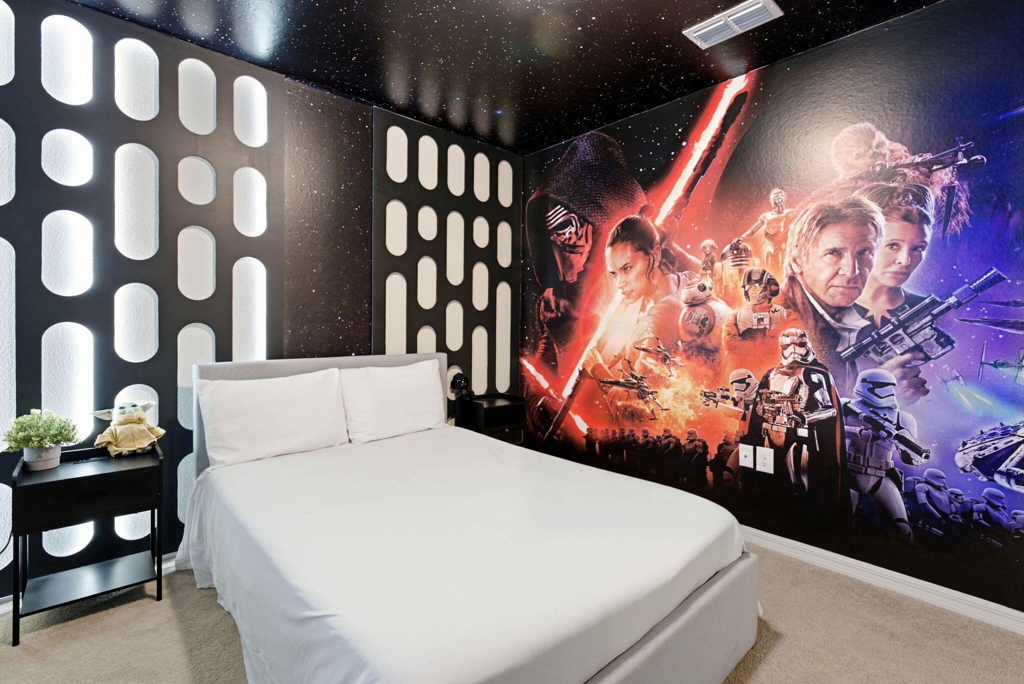 Un dormitorio con un mural con temática de Star Wars, una cama, una mesita de noche y una planta en maceta.