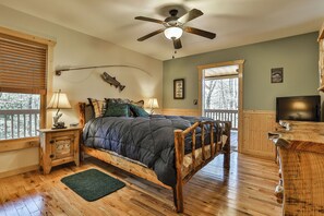 A bedroom with a wooden bed, a ceiling fan, a TV, and a window with blinds. - Mountain Escape - Hot Tub, Fire Pit, Games & 3 Scenic Decks (Ellijay)