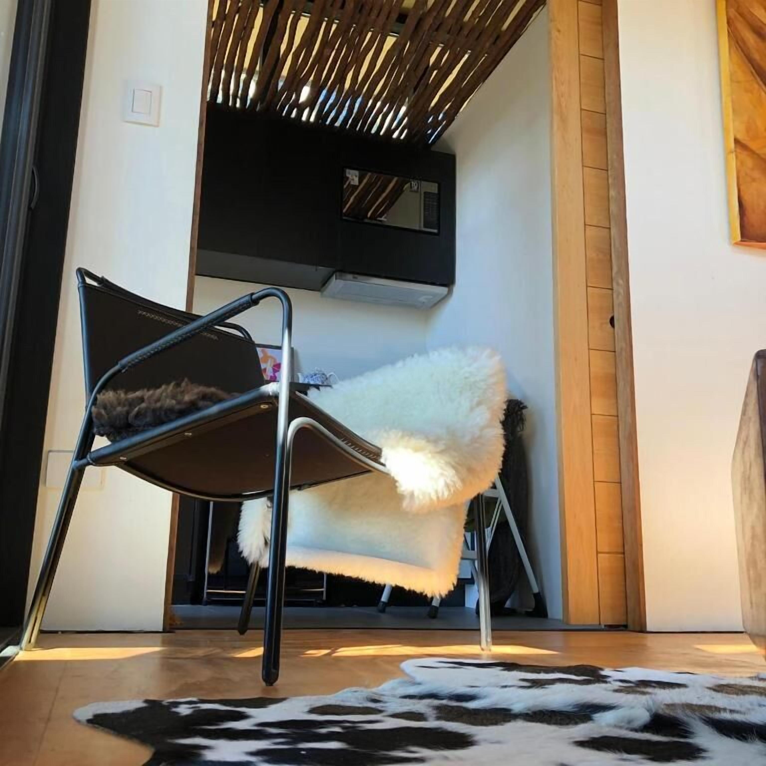 Una habitación con una silla de metal negro, una silla blanca de pelo y un tapete de cuero de vaca.