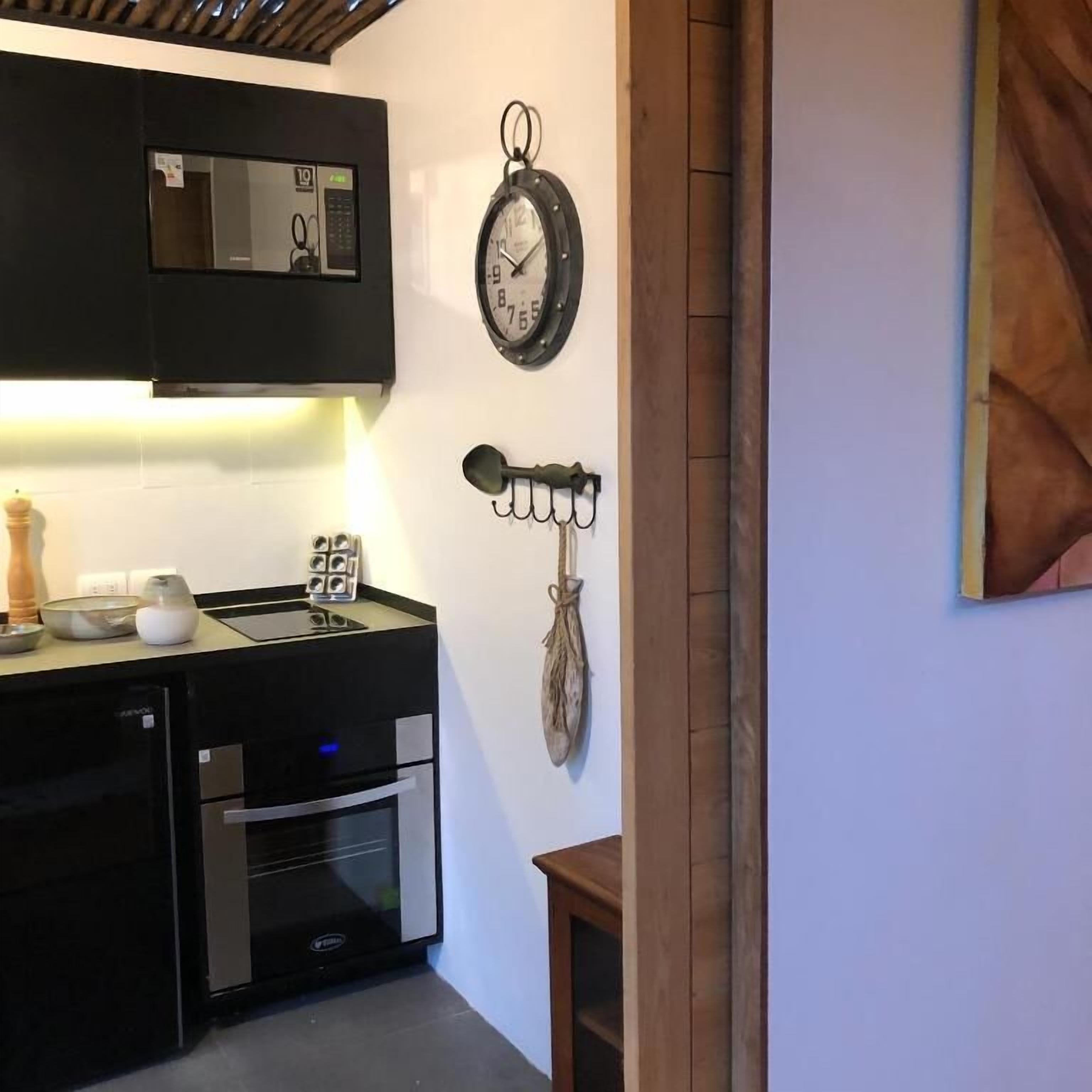 Una cucina con forno a microonde, forno e lavello. C'è una sveglia a muro e un portachiavi appeso al muro.